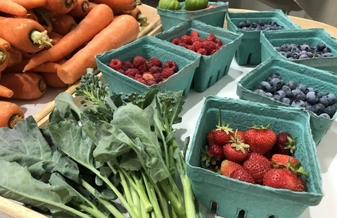 A counter with leafy vegetables, carrots, strawberries and blueberries