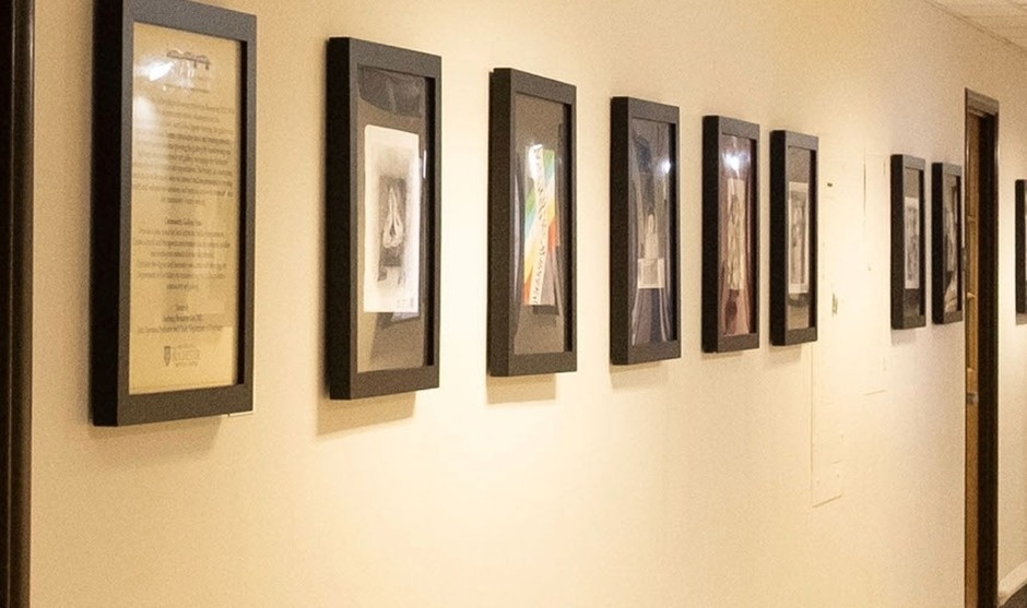 Hallway gallery (sign reads 'Gallery') with framed art on left and a group of people at the far end.