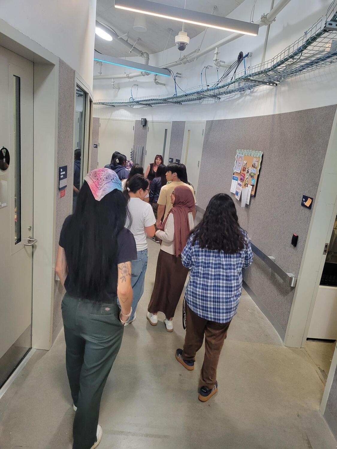 Several people walking down a curved indoor corridor that is a back of a music venue