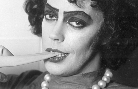 A performer in drag makeup and a pearl necklace bites a piece of fabric.