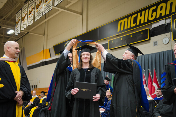 Advisors hooding a PhD candidate at commencement.