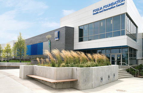 Exterior of the Health and Recreation Center, showing a white and gray building with a windowed entry way and tall grasses out front.